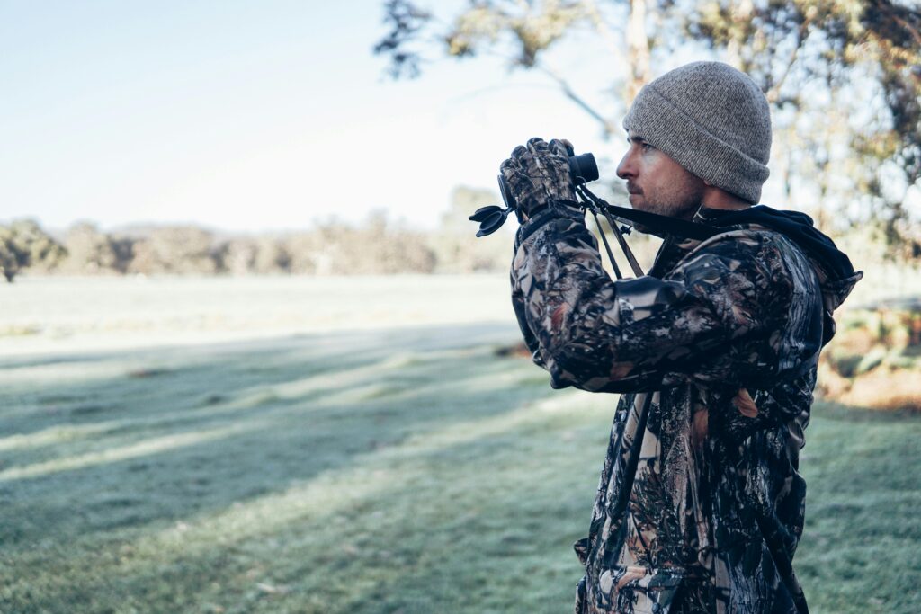 Adult male in camouflage outfit using binoculars in an open field, showcasing outdoor exploration and observation.